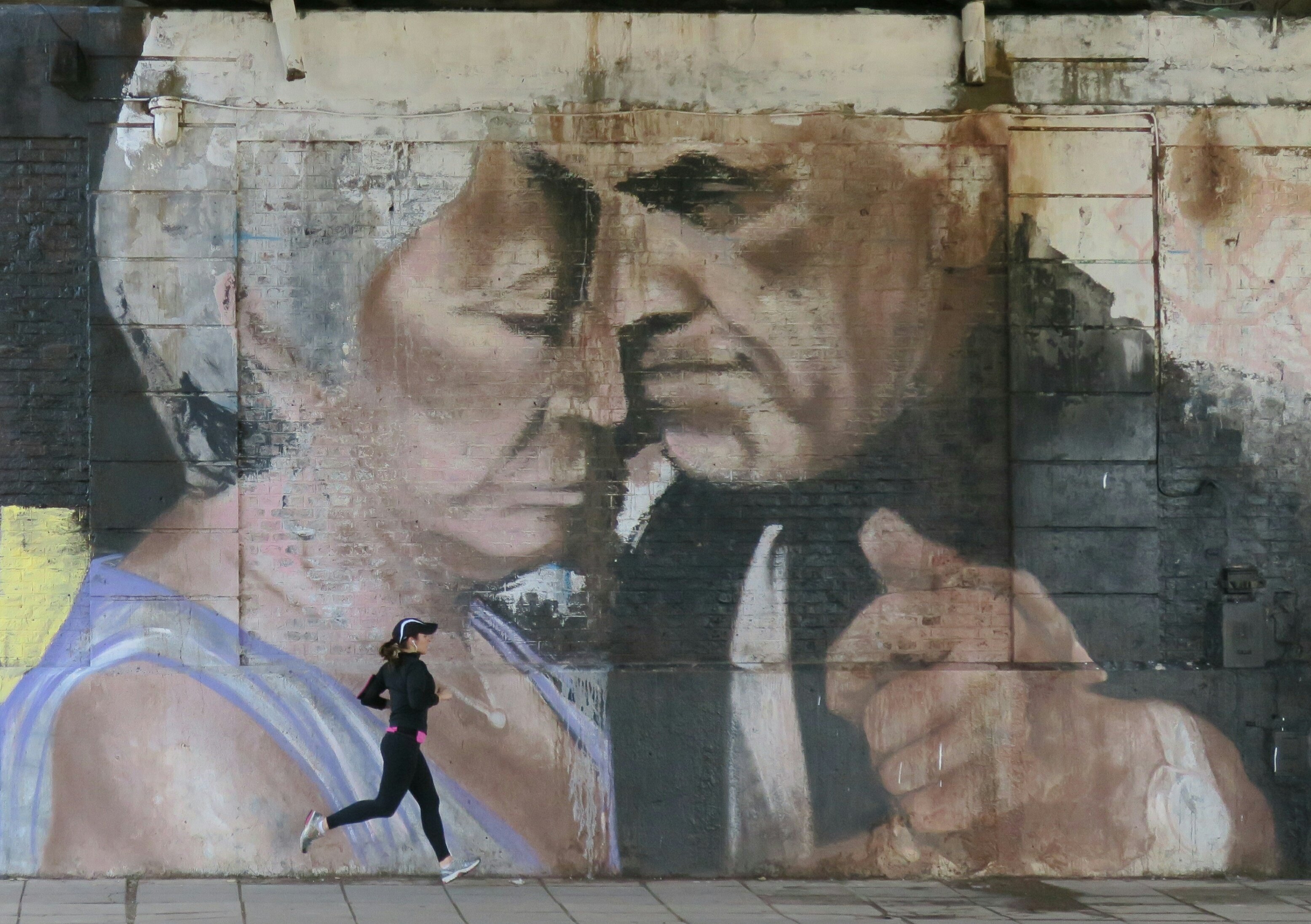 BAS01. BUENOS AIRES (ARGENTINA), 31/07/2016.- Fotografía del 28 de julio de 2016, de una mujer corriendo junto a un fragmento del mural pintado por el artista argentino Alfredo Segatori, en Buenos Aires (Argentina). El bandoneón, la tradicional milonga, Carlos Gardel, la pasión en el tango y su vínculo con las carreras de caballos componen un mural que ha trasladado el ritmo del 2x4 hasta las mismas paredes de Buenos Aires. Un homenaje producto de los aerosoles del artista argentino Alfredo Segatori. EFE/Irene Valiente