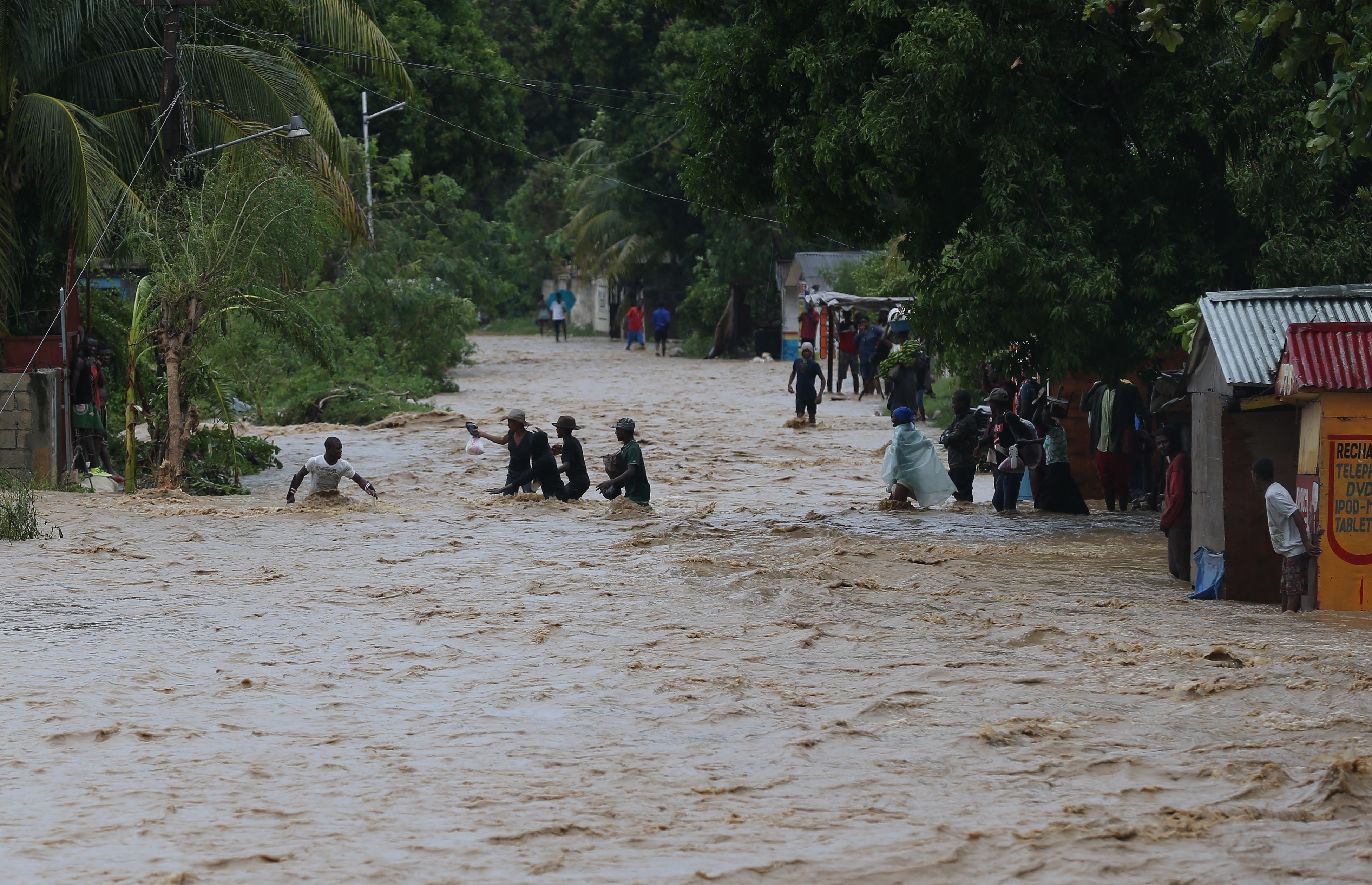 HAI01. LEOGANE (HAITI), 05/10/16.- Personas intentan cruzar una calle inundada tras el paso del huracán Matthew hoy, 5 de octubre de 2016, en Leogane (Haití). El poderoso huracán de categoría 4 Matthew continúa su ruta con vientos máximos de 140 millas por hora (220 km/h). La región sur de Haití sigue hoy incomunicada por los estragos causados por el poderoso huracán Matthew, que azotó el país este martes y causó al menos nueve muertos. EFE/Orlando Barría