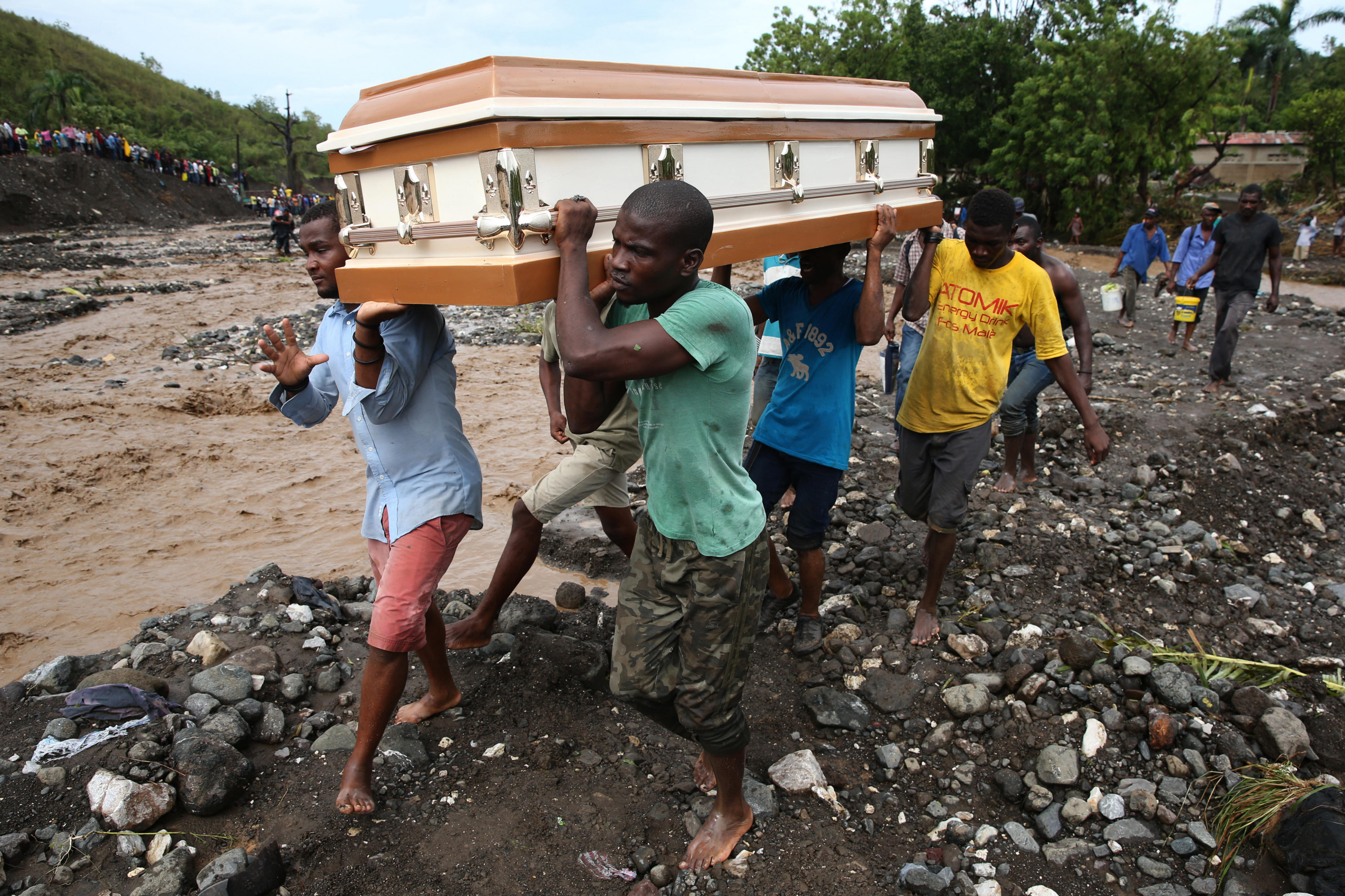 HAI01. PETIT GOAVE (HAITI), 05/10/16.- Varios hombres cargan un ataúd e intentan cruzar el río La Digue, debido al derrumbe del único puente que conecta con el sur, tras el paso del huracán Matthew hoy, 5 de octubre de 2016, en Petit Goave (Haití). El impacto del huracán Matthew en Haití, donde dejó al menos nueve muertos, miles de desplazados y comunidades incomunicadas, principalmente en el suroeste, obligó hoy a las autoridades electorales a aplazar los comicios del domingo. EFE/Orlando Barría