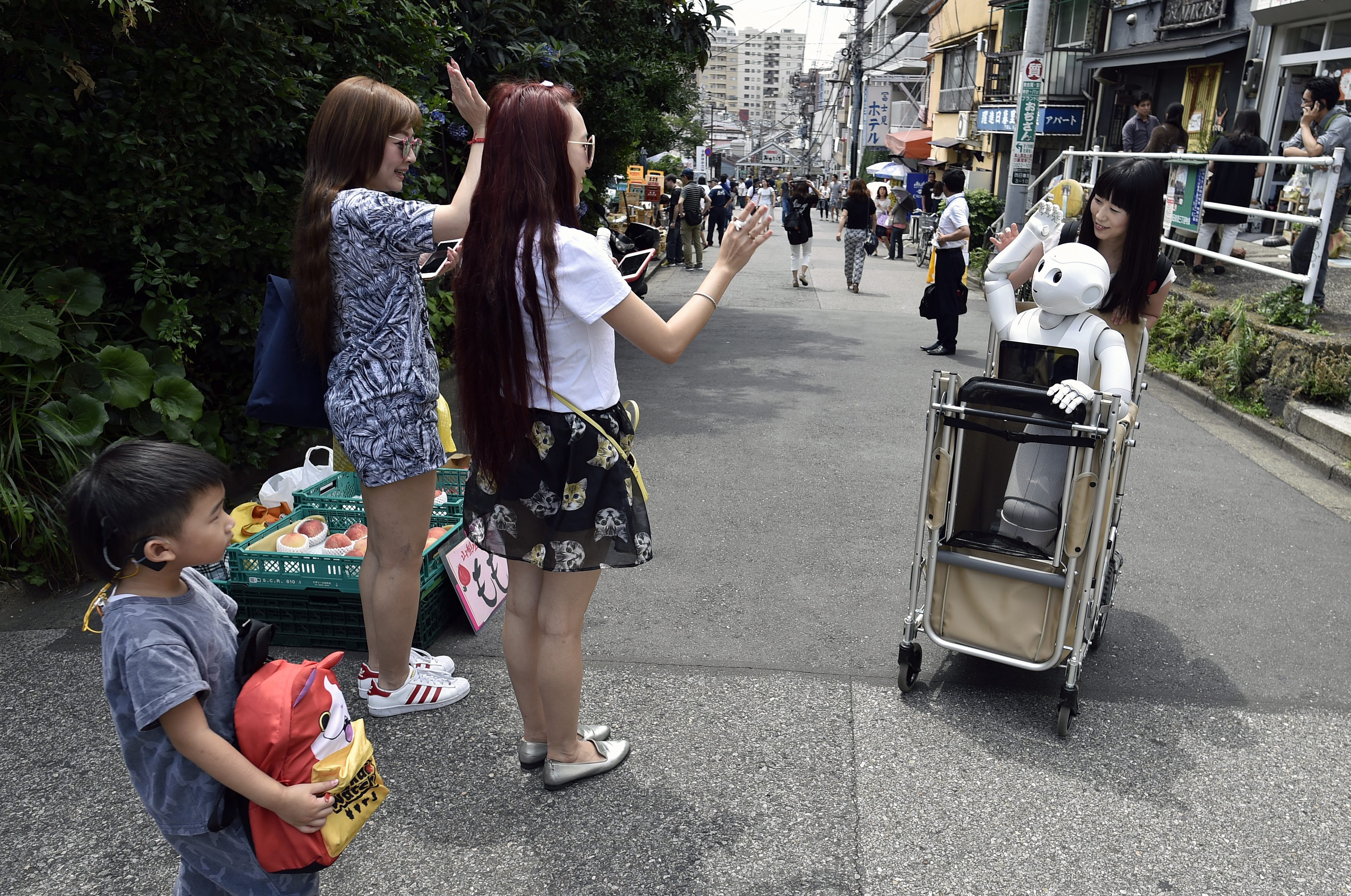 FRA47. Tokyo (Japan), 25/06/2016.- (18/21) Tourists react as they see Tomomi Ota (R) pushing a cart loaded with her humanoid robot Pepper in Tokyo, Japan, 26 June 2016. Reaching 120cm in height and 28 kilograms in weight, Pepper does not enter in the category of 'Äòportable'Äô robot. But those characteristics don'Äôt stop Tomomi Ota to take Pepper in a cart to stroll in her neighborhood, go shopping or even take the subway. In June 2014, when Pepper was presented for the first time by Japanese telecommunications and Internet corporation Softbank at a press event, Tomomi looked at the presentation via a live broadcast on Ustream. While some people were 'Äòscared'Äô or reluctant by the new humanoid robot, curiosity pushed her to apply to lottery sales for the first lot of 200 Pepper. She was lucky enough to acquire then a 'ÄòDeveloper'Äôs Pepper'Äô, the first models of the robots which need to be programmed by the users. Pepper entered Tomomi'Äôs home in November 2014 and was soon adopted by her parents to become a member of the family. Having degrees in media design and music, Tomomi had to learn programming and her efforts deepened her bonds with her new friend. Capable of reading human emotions and to adapt to his interlocutor, the robot created by Aldebaran Robotics and SoftBank Robotics is now used as customer service in stores and 1000 units are sold out in minutes after being on sale every month. Pepper is making his way to Japanese homes but few can enjoy so much outdoor like Tomomi'Äôs one. Asked if she isn'Äôt worried about damaging her robot friend during her activities, the 30-year-old said that she is taking extra care as she couldn'Äôt imagine being separated two months from Pepper, the average time needed for a repair. (Tokio, Japón) EFE/EPA/FRANCK ROBICHON PLEASE REFER TO THE ADVISORY NOTICE (epa05406529) FOR FULL PACKAGE TEXT